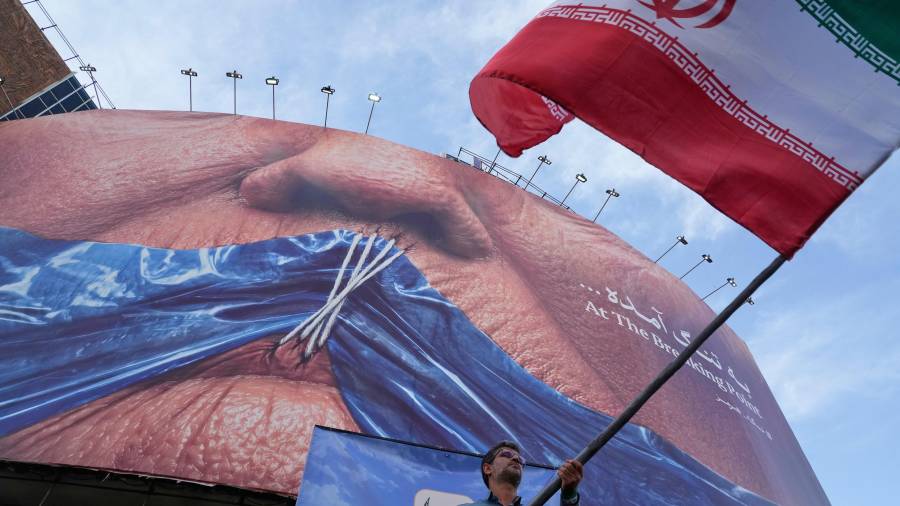 Un hombre ondea una bandera iraní para una campaña progubernamental bajo un cartel que muestra el estrecho de Ormuz y los labios del presidente de Estados Unidos, Donald Trump en una Teherán, Irán.
