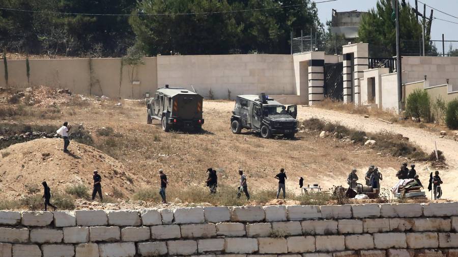 Soldados israelíes hacen guardia junto a colonos frente a viviendas palestinas que estos bloquearon en la localidad de Qusra, al sur de Nablus, en la ocupada Cisjordania, el 12 de agosto de 2026.