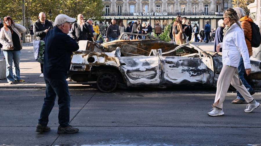 Gente mira a un auto calcinado en Place de la Republique el día después de una manifestación contra el creciente coste de la vida, que se suma a las protestas estudiantiles, en París.