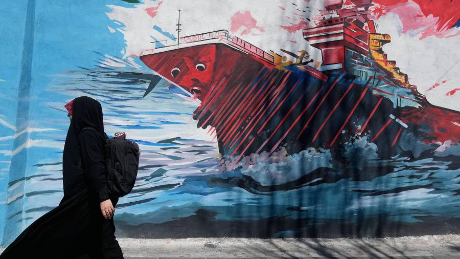 Una mujer pasa junto a un mural que muestra un portaaviones estadounidense bajo ataque en el centro de Teherán, Irán, el lunes 8 de junio de 2026.