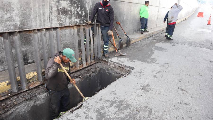 Trabajadores retiran lodo y basura acumulada en una rejilla pluvial del paso a desnivel en el periférico.