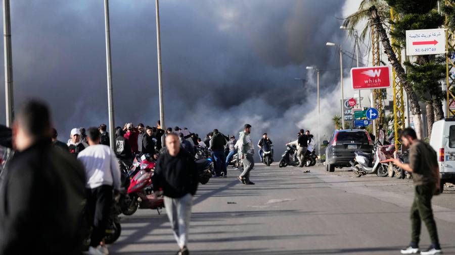 El humo se eleva mientras los transeúntes observan tras un ataque israelí que impactó un edificio cerca de la carretera del aeropuerto en Beirut.