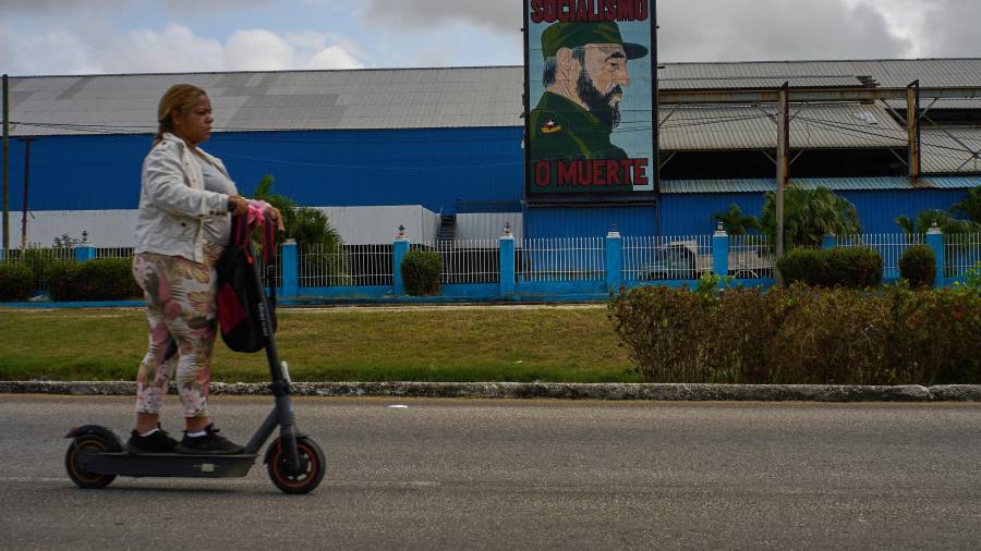 Una mujer pasa en patineta eléctrica frente a una fábrica que exhibe una imagen del fallecido líder cubano Fidel Castro, con la leyenda “Socialismo o muerte”, en La Habana, Cuba.