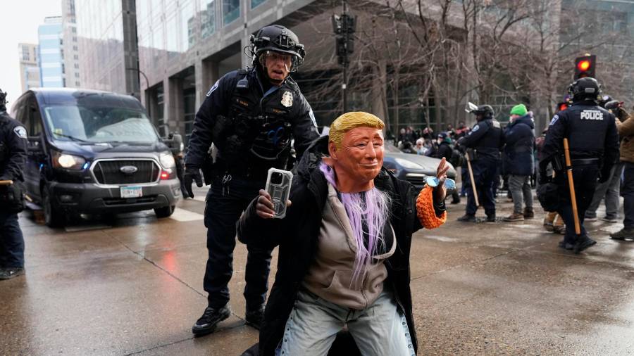 A person wearing a Trump mask is told to get up by a Minneapolis Police officer Saturday, Jan. 17, 2026, in Minneapolis. (AP Photo/Yuki Iwamura)