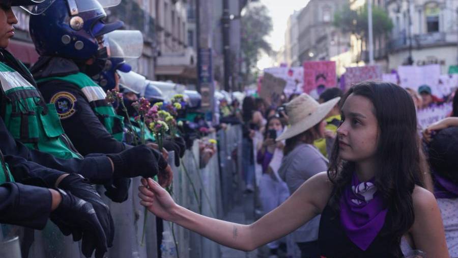 Una mujer entrega flores a la policía antidisturbios durante una marcha contra la violencia de género con motivo del Día Internacional de la Mujer, en CDMX.
