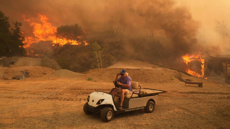 Un residente sale de su propiedad en un carrito de golf mientras el incendio Canyon arde el 7 de agosto de 2025 en Hasley Canyon, California.
