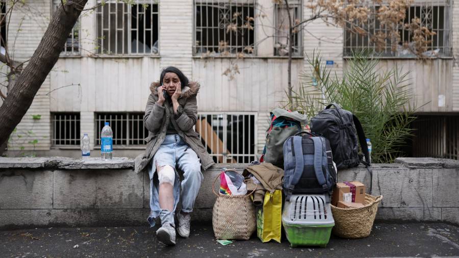 Una mujer herida habla por teléfono celular mientras está sentada junto a sus pertenencias tras abandonar su apartamento luego de un ataque que impactó un edificio residencial en Teherán, Irán.