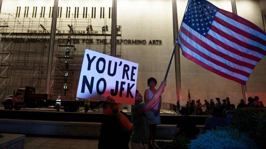 Manifestantes ondean una bandera de Estados Unidos y carteles mientras operarios se preparan para retirar el nombre del presidente Donald Trump del John F. Kennedy Center for the Performing Arts en Washington, el 13 de junio de 2026.