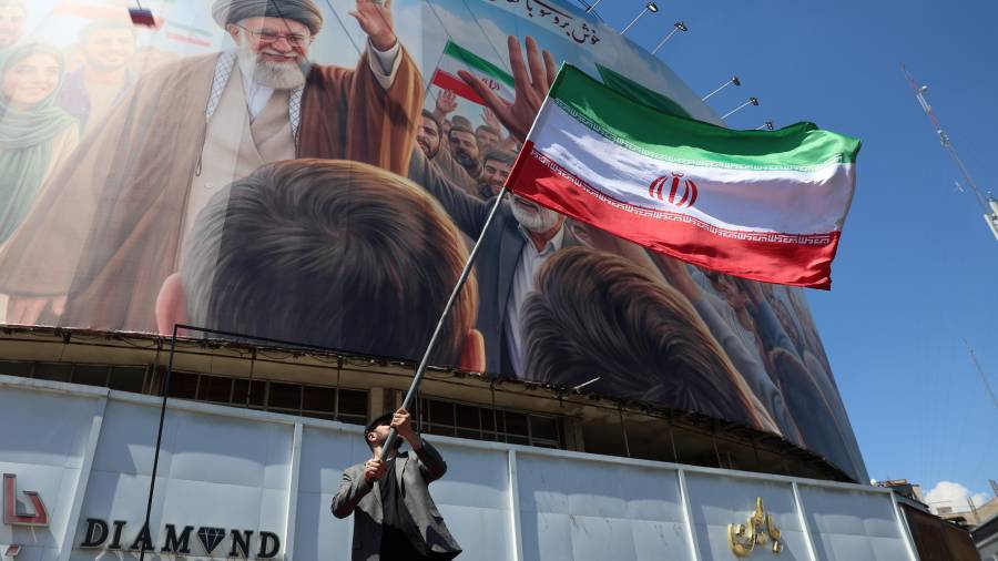 Un hombre iraní ondea la bandera nacional de Irán frente a una gran valla publicitaria que muestra un retrato del difunto líder supremo iraní, el ayatolá Ali Khamenei, en la plaza Valiasr de Teherán, Irán.