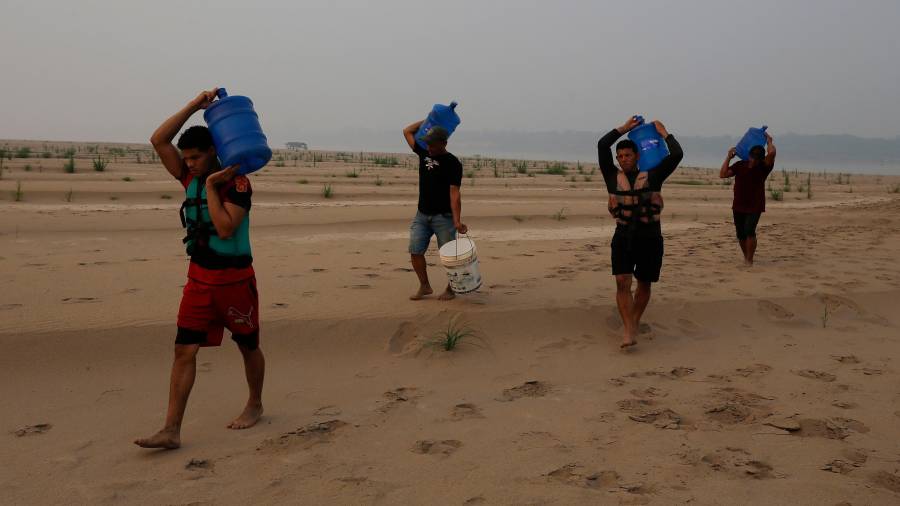 Personas llevan agua desde Humaita hacia la comunidad de Paraizinho, a lo largo de un tramo seco del río Madeira, un afluente del Amazonas, en medio de una sequía, el 8 de septiembre de 2024, en Brasil.