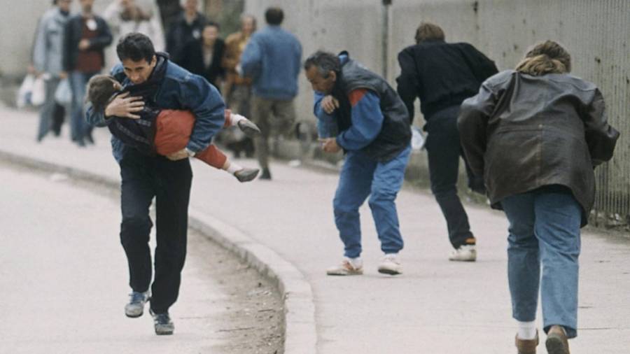 Un hombre acuna a su hijo mientras la gente pasa corriendo por uno de los peores lugares para los francotiradores en Sarajevo en abril de 1993.