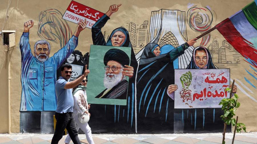 Una pareja iraní camina junto a un mural antiestadounidense e israelí en una calle de Teherán, Irán, el 8 de mayo de 2026. Irán y EUintercambiaron disparos en el estrecho de Ormuz en medio de un alto el fuego.