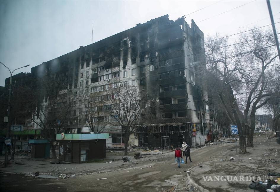 $!La gente lleva agua cerca de un edificio de apartamentos devastado y quemado en el centro de Mariupol, Ucrania.