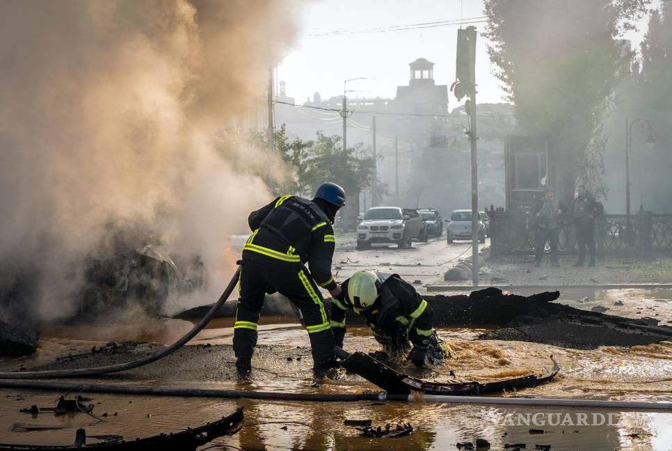 $!Un bombero ayuda a su colega a escapar de un cráter mientras apagan el humo de un automóvil quemado después de un ataque ruso en Kiev, Ucrania.