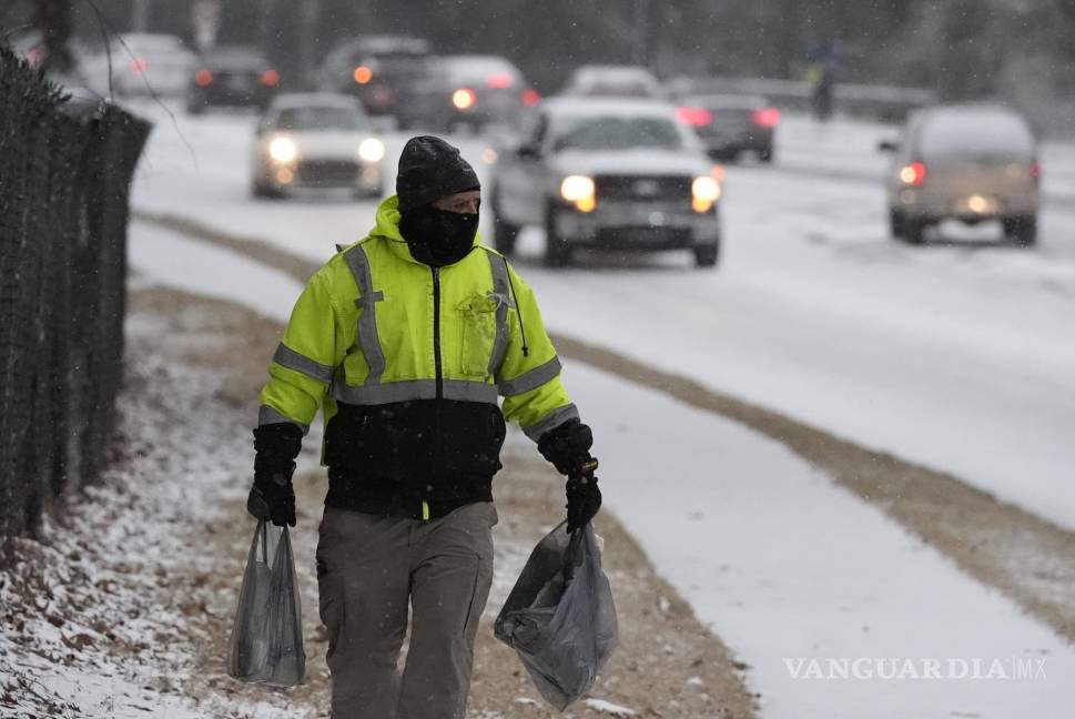 $!na persona camina por la acera con compras mientras cae nieve durante una tormenta invernal el martes 21 de enero de 2025, en Tucker, Georgia.