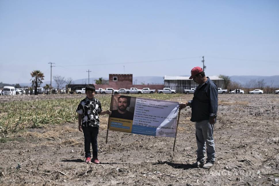 $!Dos personas sostienen una fotografía de un familiar desaparecido afuera del Rancho Izaguirre, donde se descubrieron restos óseos en Teuchitlán, Jalisco.