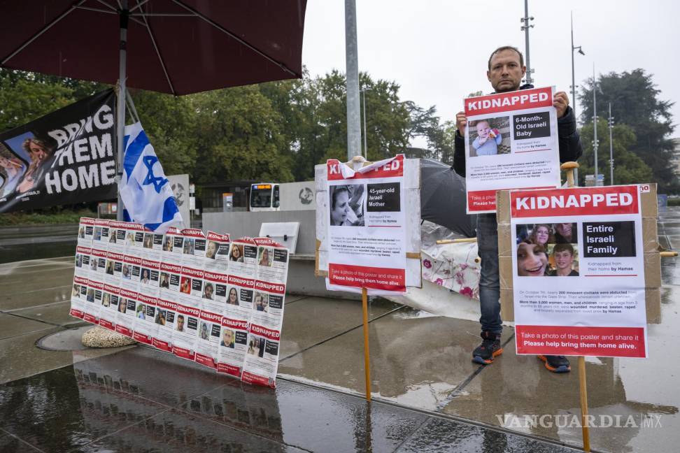 $!Un manifestante sostiene un cartel junto a pancartas con fotografías de rehenes tomados por Hamás junto a la sede europea de las Naciones Unidas en Ginebra.