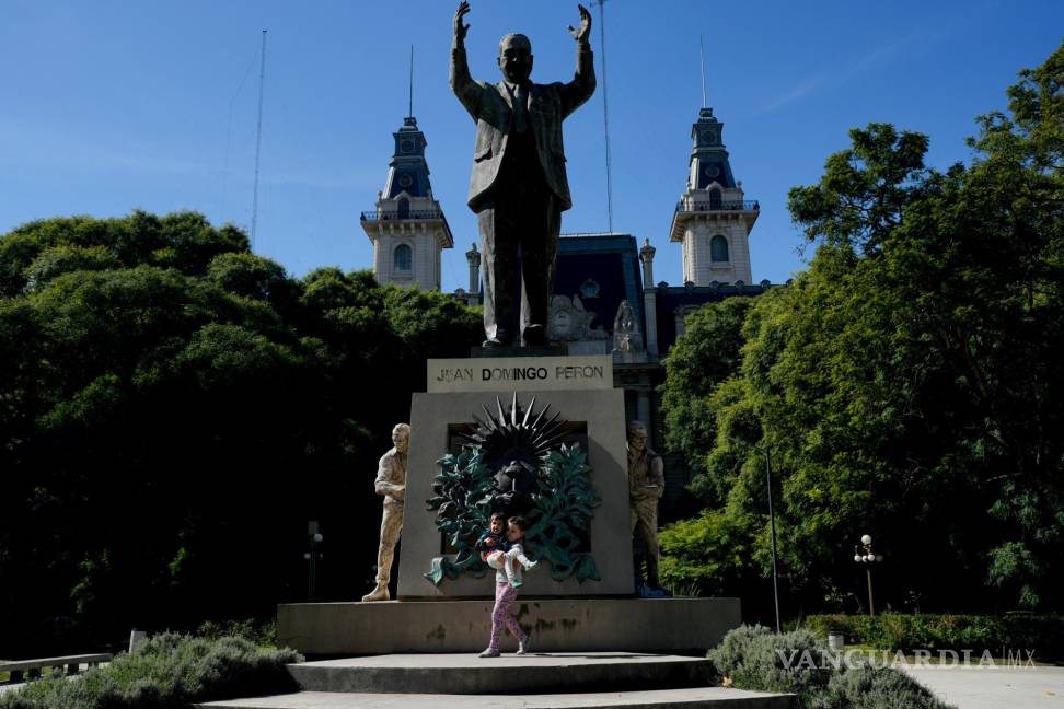 $!Aksinia Domini, de 6 años, carga a su hermanita Agata, de 3, frente a un monumento del expresidente argentino Juan Domingo Perón en Buenos Aires.
