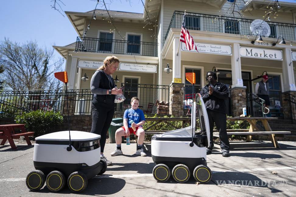 $!30 de marzo de 2020. Personas reciben comida de robots de reparto de alimentos, famosos durante la pandemia, en el mercado Broad Branch Market en Washington.