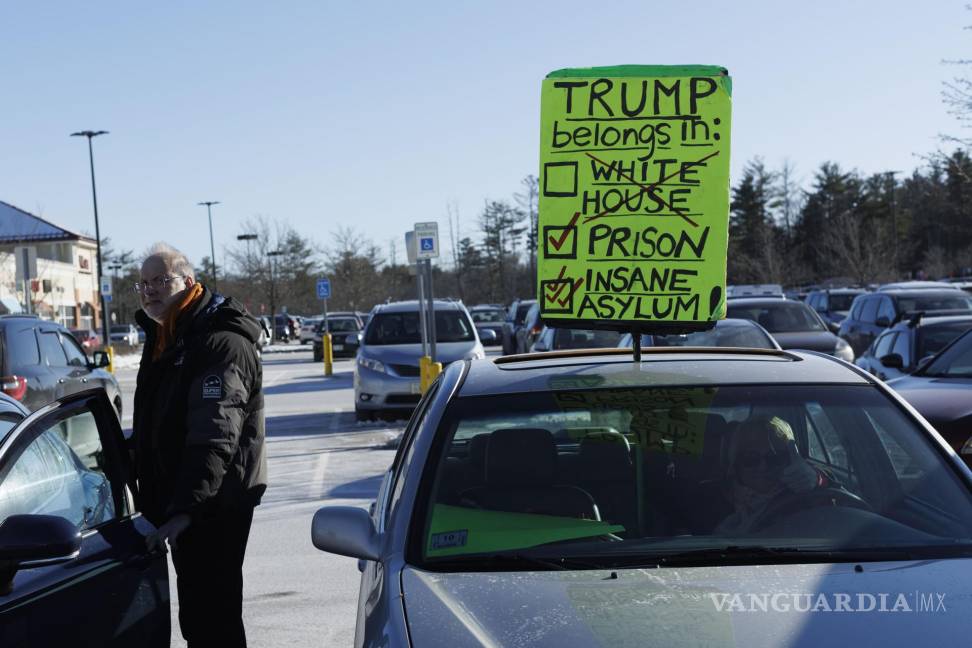 $!Una mujer sostiene un cartel en el techo de su vehículo en protesta contra el expresidente Donald Trump afuera en New Hampshire.