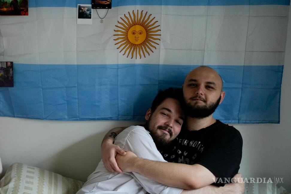 $!Los rusos Dmitri Yarin, a la izquierda, y su pareja Nikolai Shushpan, se abrazan frente a una bandera argentina en su casa en Buenos Aires, Argentina.