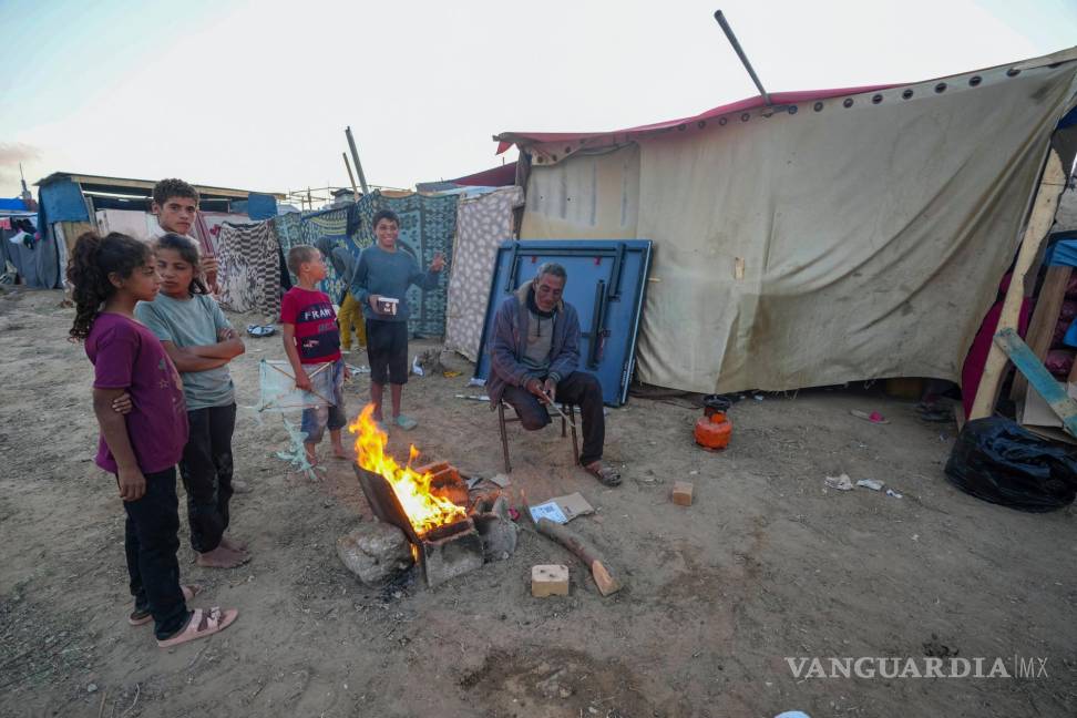 $!Un hombre palestino se sienta junto a una fogata junto con otros niños frente a tiendas de campaña improvisadas en el campamento de Deir al Balah.