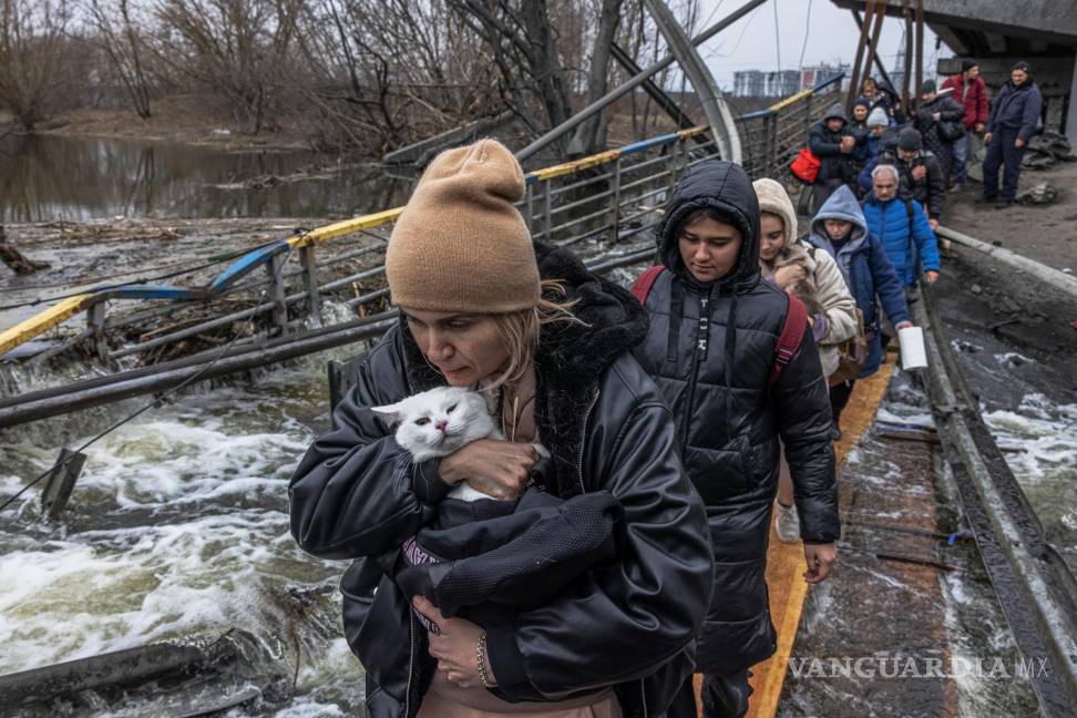 $!Una mujer con su gato cruza un puente destruido mientras los residentes huyen desde el frente de la ciudad de Irpín, en Kiev. EFE/Roman Pilipey