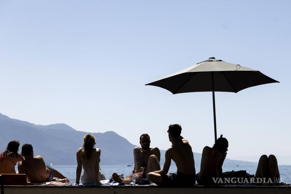 $!La gente descansa bajo una sombrilla en un cálido día de verano a orillas del lago de Ginebra, frente a las montañas de los Alpes suizos, en Vevey, Suiza.