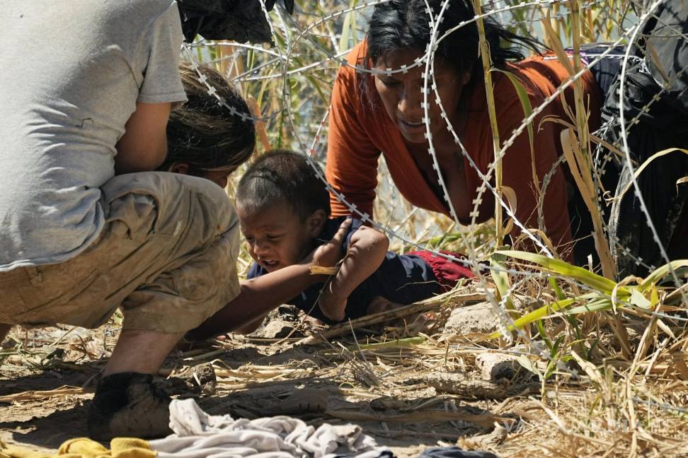 $!Migrantes logran cruzar a un niño por debajo de una alambrada de púas, en la frontera de Eagle Pass y Piedras Negras.
