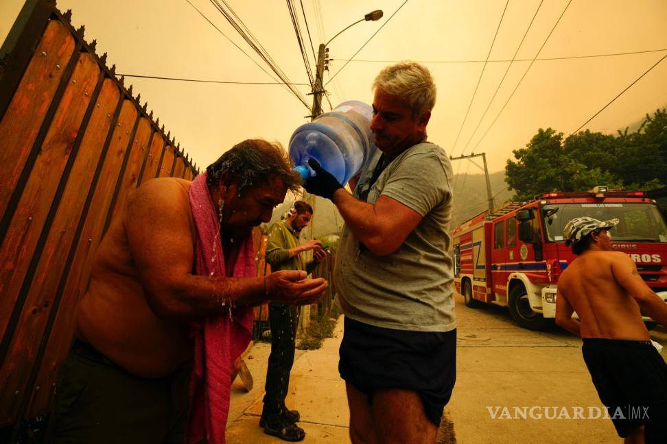 $!Un hombre ayuda a un vecino a refrescarse con una botella de agua mientras los incendios avanzan en el entorno, en Viña del Mar, Chile.