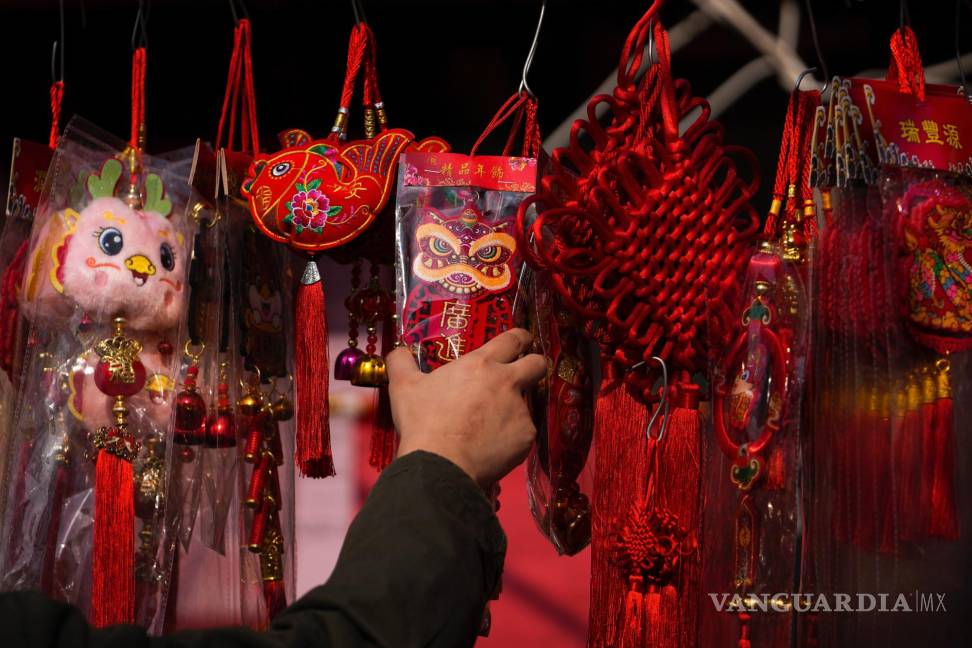 $!Un hombre elige un ornamento para atraer la prosperidad en un puesto de un mercado en la víspera del Año Nuevo Lunar, en Beijing.