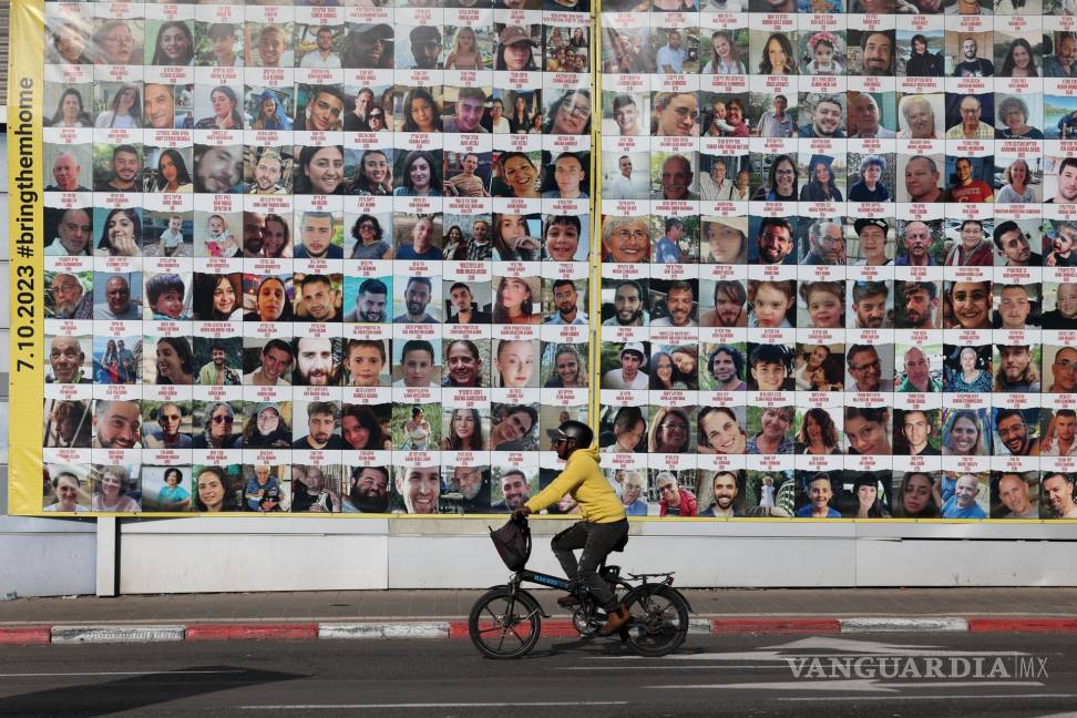 $!Una persona pasa en bicicleta junto a un cartel que muestra imágenes de rehenes israelíes retenidos por Hamás en Gaza, en Tel Aviv, Israel.