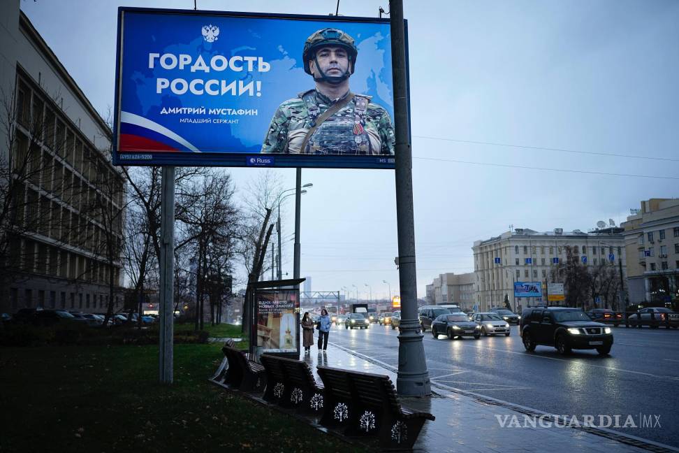 $!Dos mujeres están paradas en una parada de autobús con un cartel que dice “Orgullo de Rusia” de un soldado ruso en Moscú, Rusia.