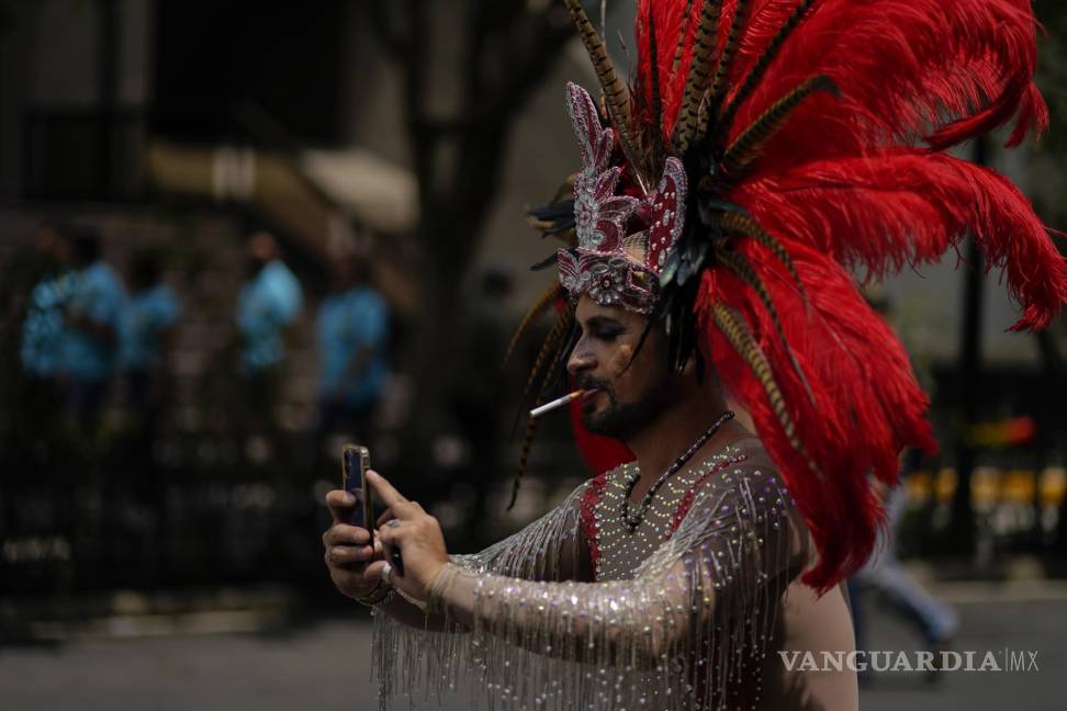 $!Un participante, con un tocado azteca y fumando un cigarrillo, posa para una selfie mientras participa en la marcha anual del Orgullo en la Ciudad de México.