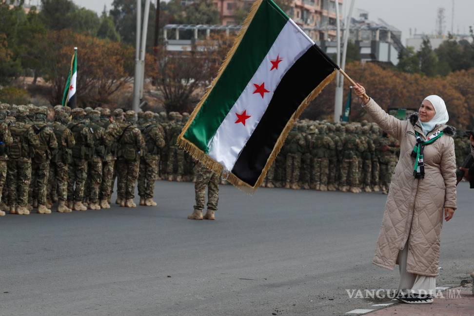 $!Una mujer y miembros del nuevo ejército sirio se forman antes del desfile militar por las celebraciones del año del derrocamiento del expresidente Bashar al-Assad