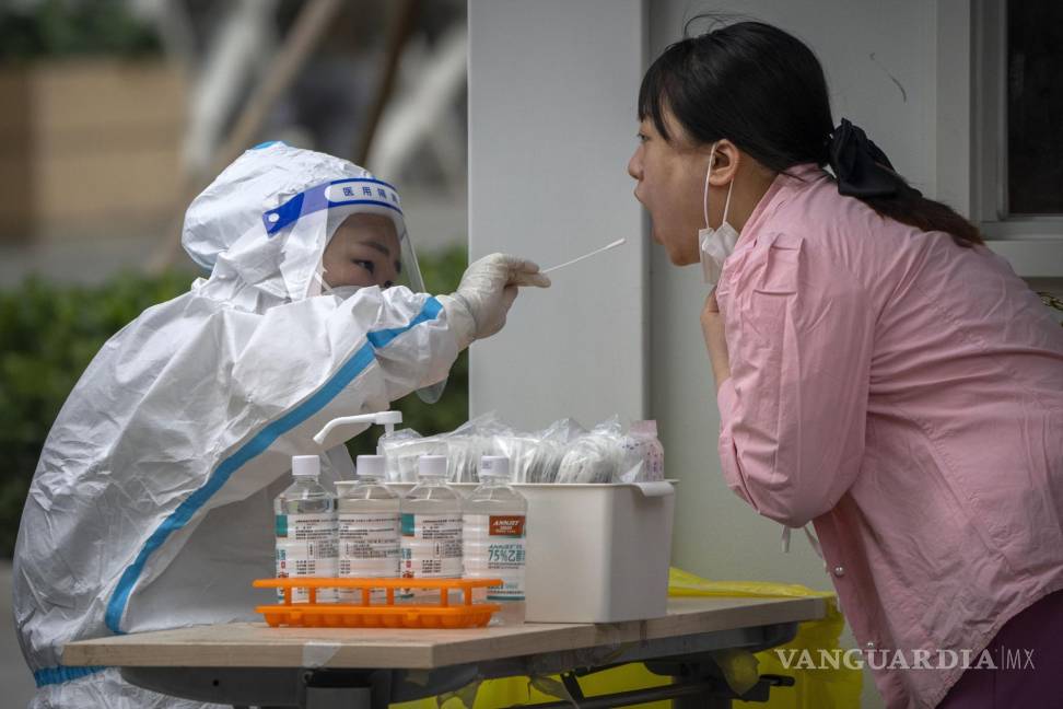 $!Una trabajadora con un traje de protección toma muestras a una mujer para una prueba de COVID-19 en Beijing.