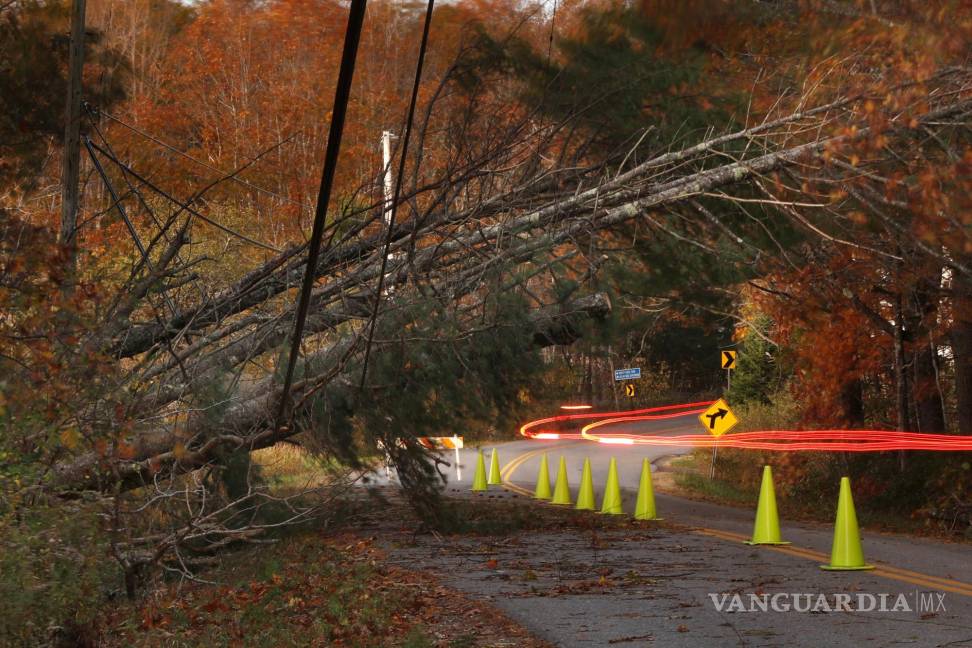$!Un automóvil deja un rastro de luz al pasar por debajo de las líneas eléctricas afectadas por los árboles derribados en Freeport, Maine.
