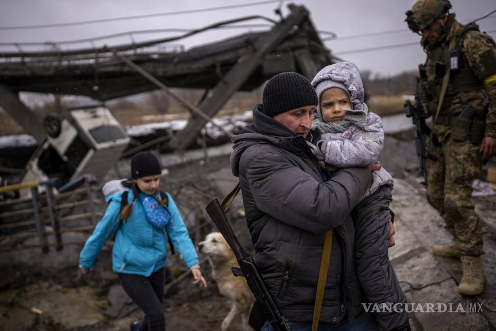 $!El miliciano local Valery, de 37 años, ayuda a una familia que huye junto a un puente destruido por fuego de artillería a las afueras de Kiev. AP/Emilio Morenatti