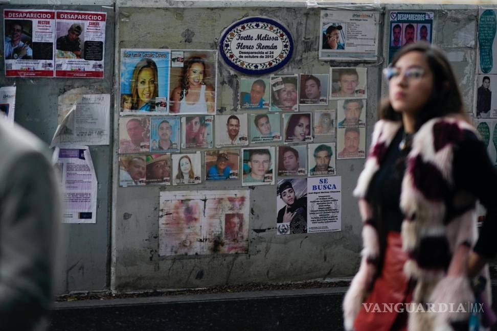 $!Una mujer pasa frente a fotografías de personas desaparecidas frente a la Procuraduría General de Justicia, en Ciudad de México.
