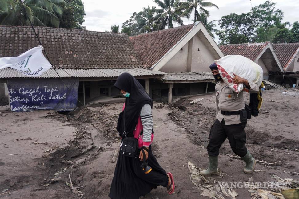 $!Un oficial de policía lleva un saco mientras ayuda a un aldeano a buscar víctimas en una aldea enterrada en cenizas volcánicas de la erupción del monte Semeru.EFE/EPA/AMMAR