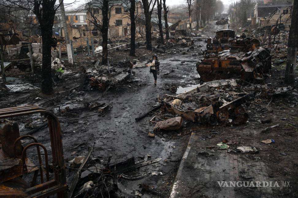 $!Una mujer pasa por una calle llena de restos de vehículos militares destruidos en Bucha, a las afueras de Kiev, Ucrania, el domingo 3 de abril de 2022.