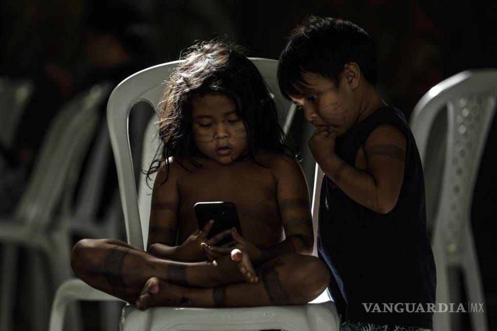 $!Una niña y un niño indígena miran un teléfono en el Parque de Igarapé en la ciudad de Belém, estado de Pará (Brasil).