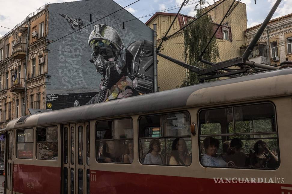$!La gente viaja en un tranvía frente a un mural llamado “El fantasma de Kyiv”, dedicado a los pilotos de la fuerza aérea ucraniana.