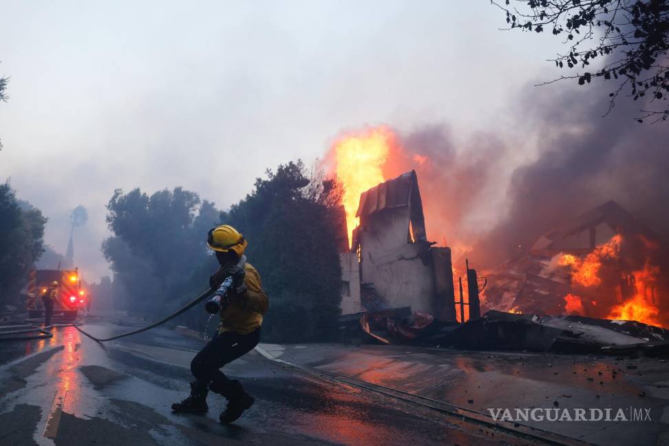 $!Un bombero intenta contener el avance de un incendio que consume una estructura en Pacific Palisades, el martes 7 de enero de 2025, en Los Ángeles.