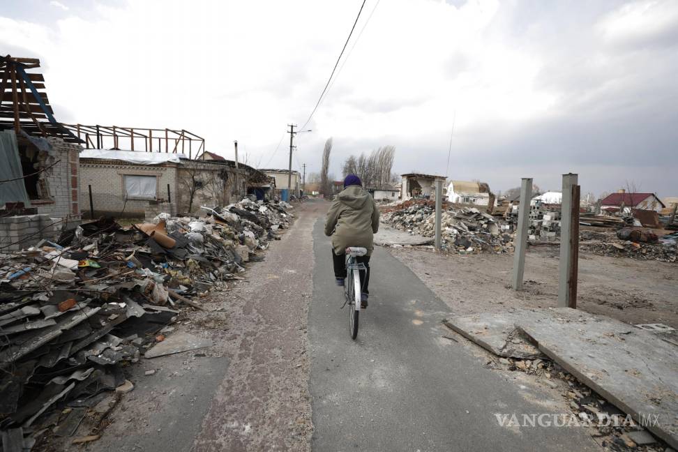 $!Una mujer monta en bicicleta frente a las casas dañadas después de un ataque aéreo ruso en el pueblo de Ulica Szkolna, óblast de Kiev.