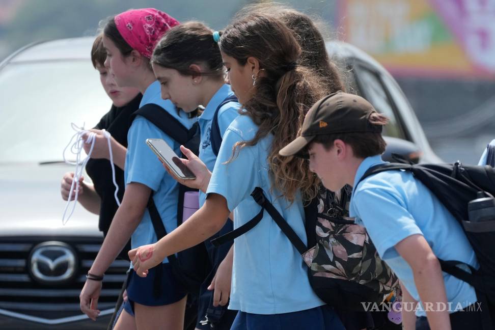 $!Una colegiala usa su teléfono mientras camina con un grupo de niños en Sídney, el lunes 8 de diciembre de 2025.