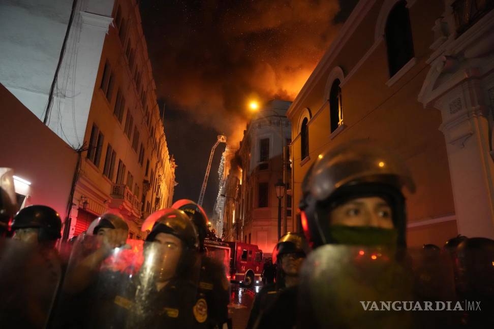 $!Policías antimotines bloquean una calle mientras un edificio arde a sus espaldas en una jornada de enfrentamientos contra manifestantes opositores en Lima, Perú.