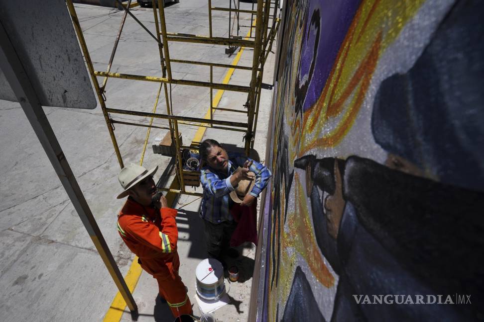 $!El artista mexicano Jesús Rodríguez(d) instruye a Luis Manuel Vélez frente a un mural que Rodríguez está pintando en la fachada de un auditorio en San Salvador.