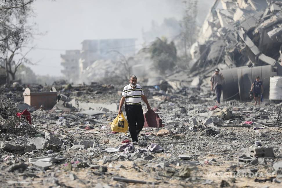 $!Palestinos caminan entre edificios destruidos por bombardeos israelíes sobre al-Zahra, a las afueras de la Ciudad de Gaza, el 20 de octubre de 2023.