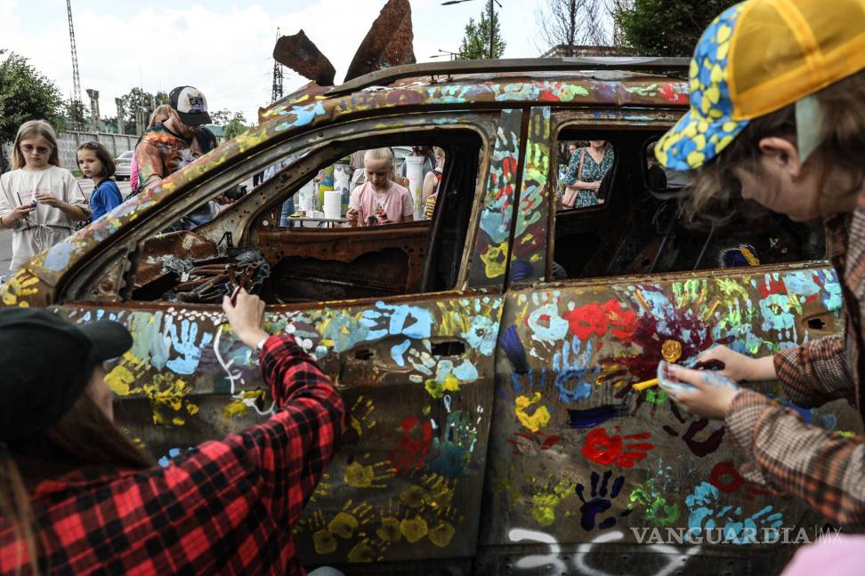 $!Artistas pintan junto a un grupo de niños coches quemados durante los combates entre las tropas ucranianas y rusas, este viernes en Bucha, Ucrania.